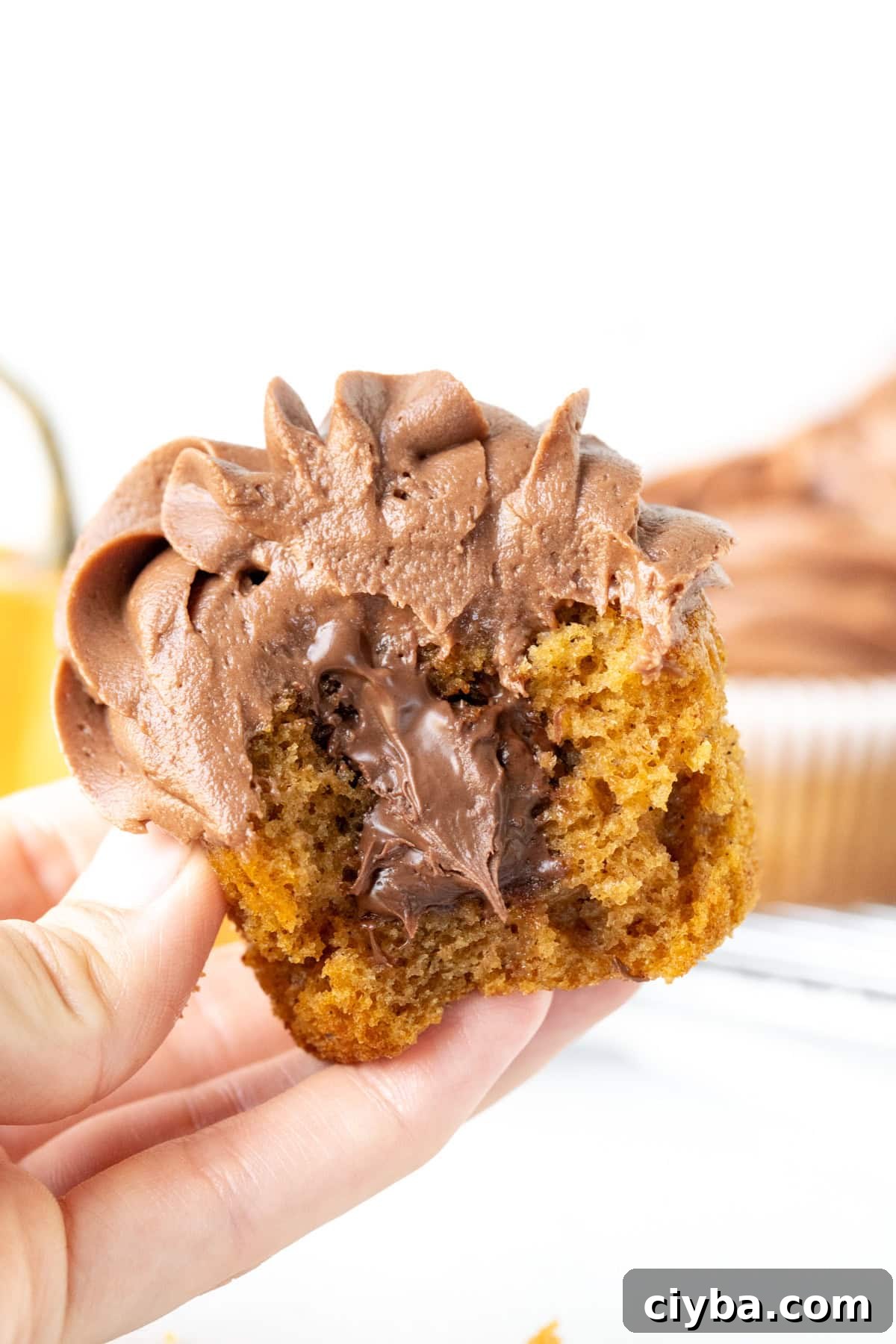 Nutella Pumpkin Cupcakes Recipe with Spiced Cream Cheese Frosting 5 Nutella pumpkin cupcake with a bite taken out and oozing with Nutella, held in a hand