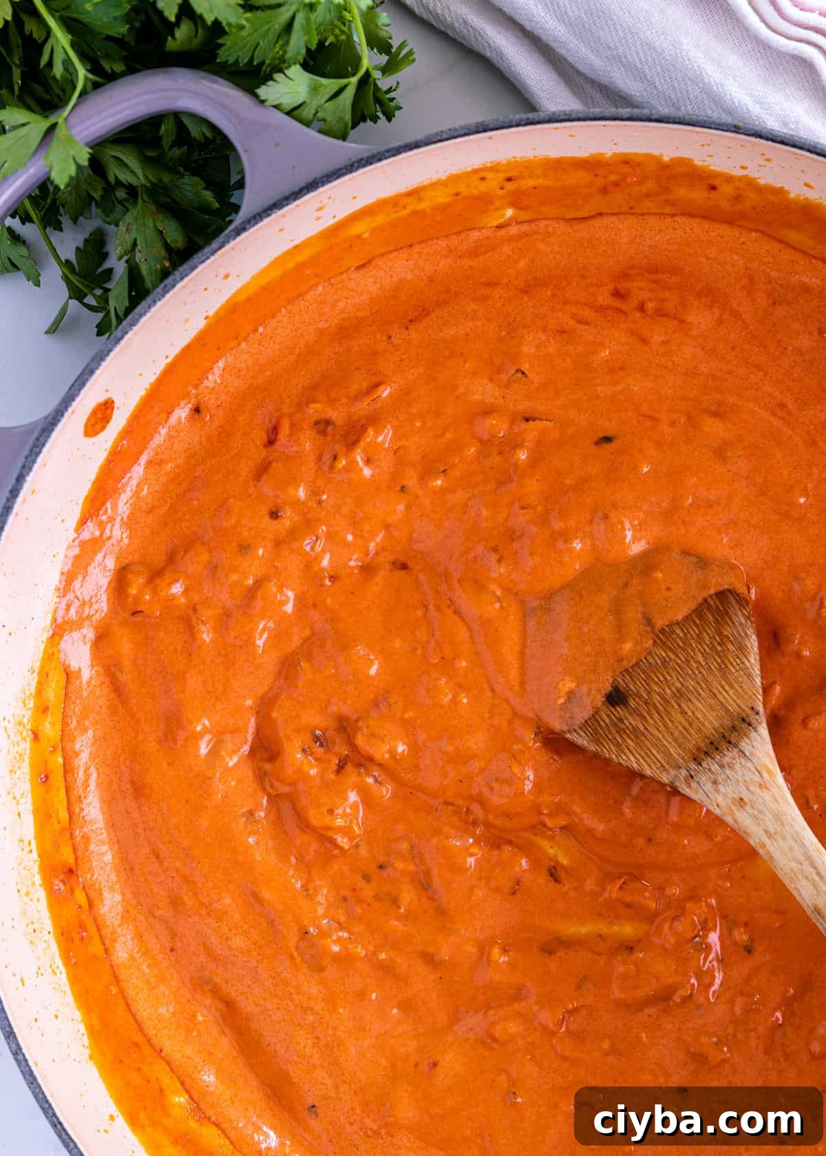 overhead: wooden spoon sitrring a big pot of vodka sauce recipe