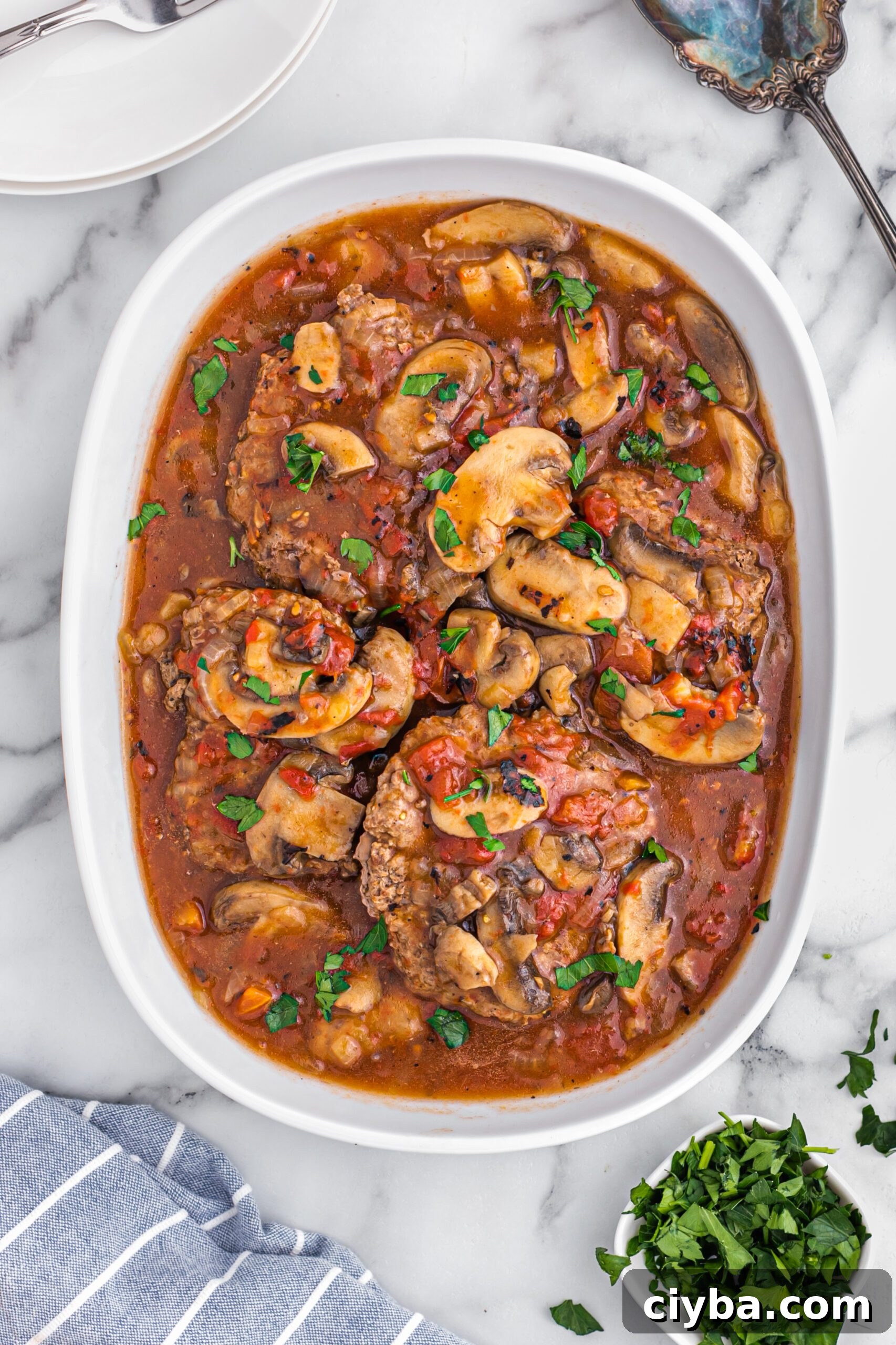 Cooked cube steak with tomatoes and mushrooms in a casserole dish.