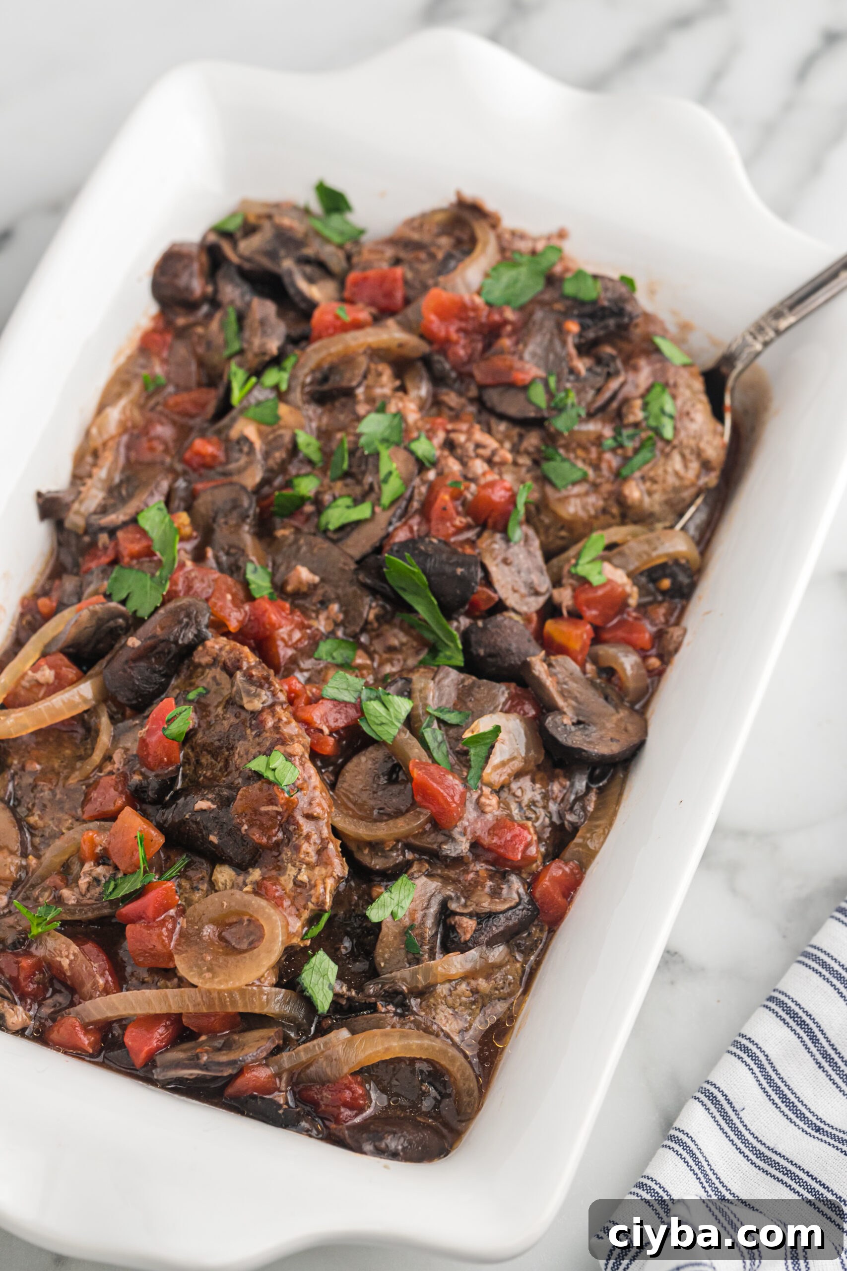 Cooked cube steak with tomatoes and mushrooms in a baking dish.