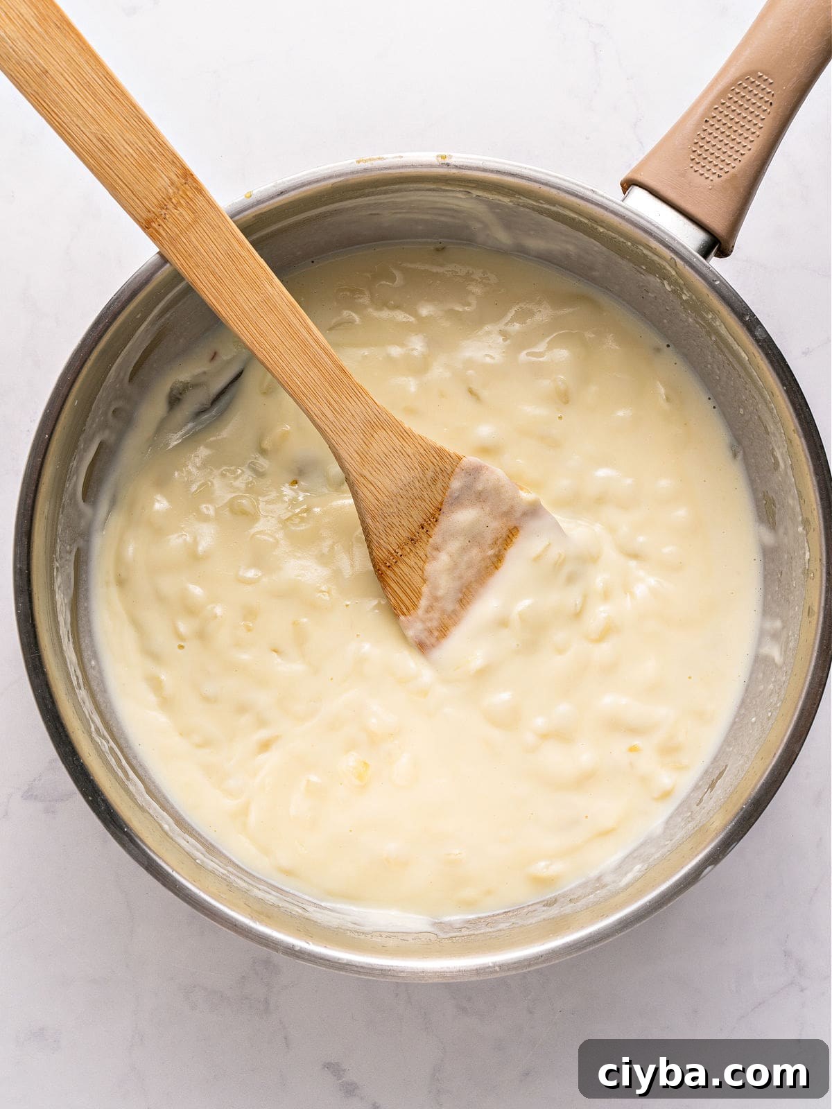 White sauce with onion in a metal saucepan. White background.