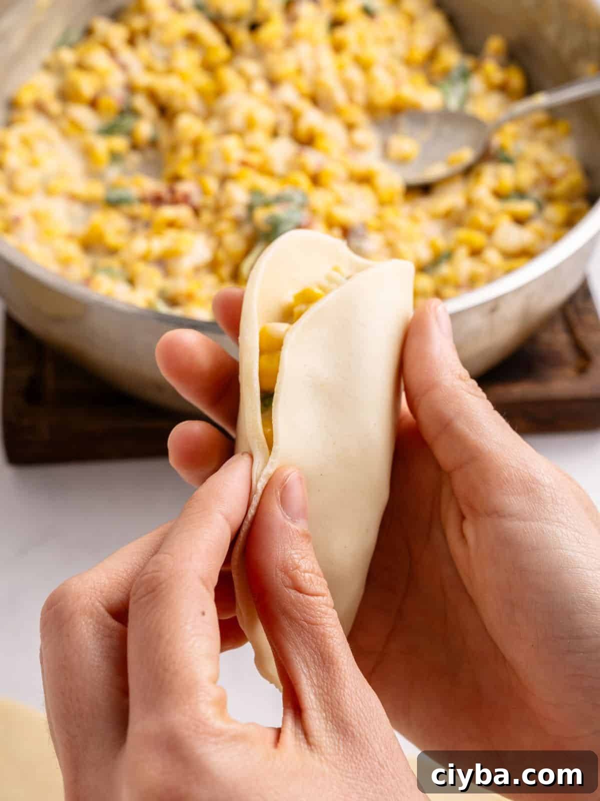 Hands closing corn empanada. Filling in skillet in the background.