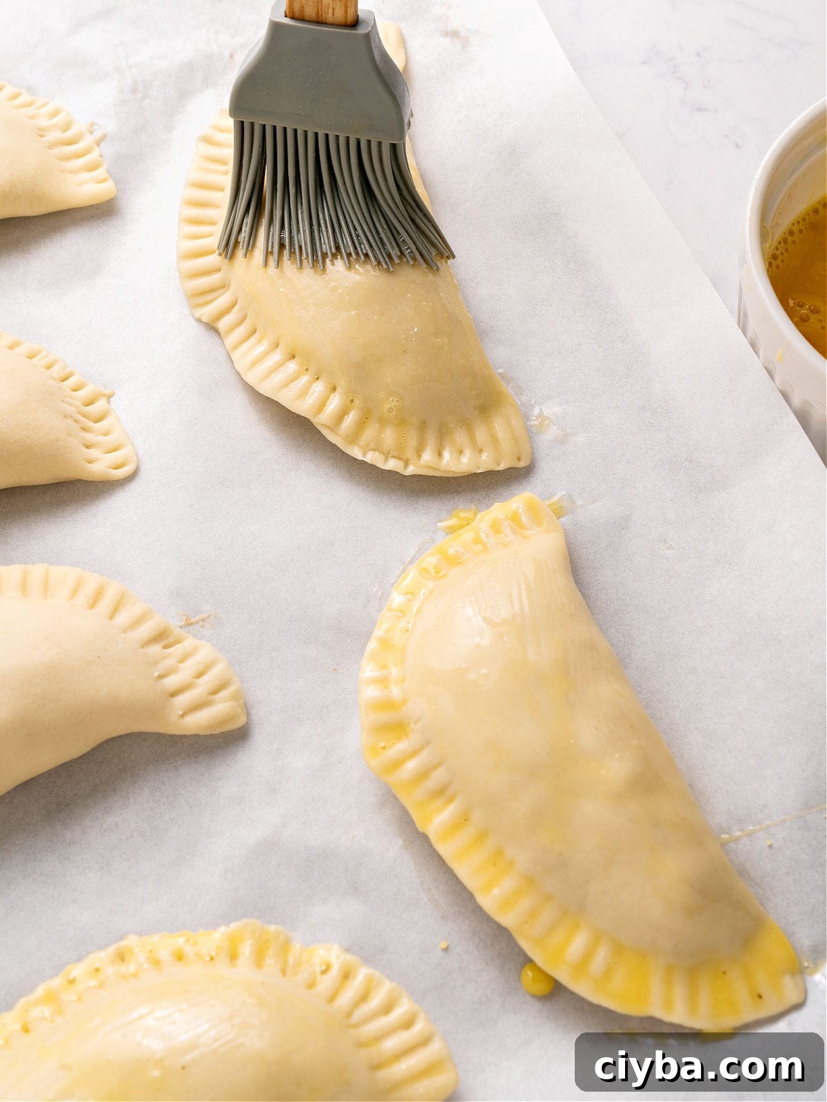Brushing empanadas on parchment paper with egg wash.
