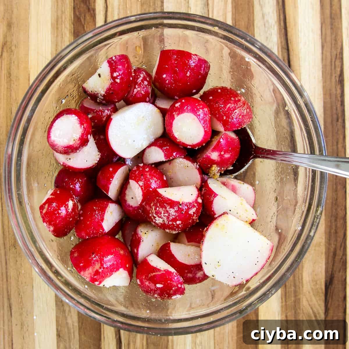 Sliced radishes in a glass bowl being tossed with oil and seasonings.