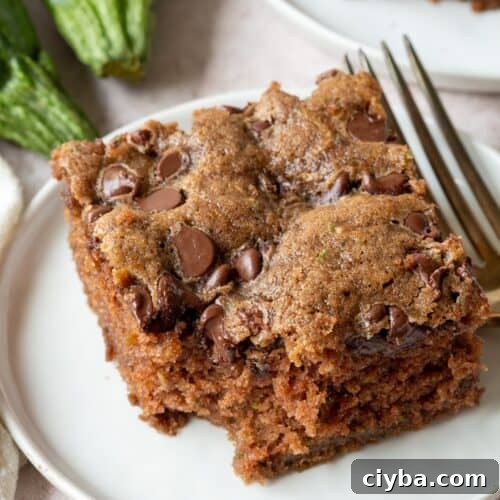 slice of chocolate chip zucchini cake with a bite taken out on a white plate.
