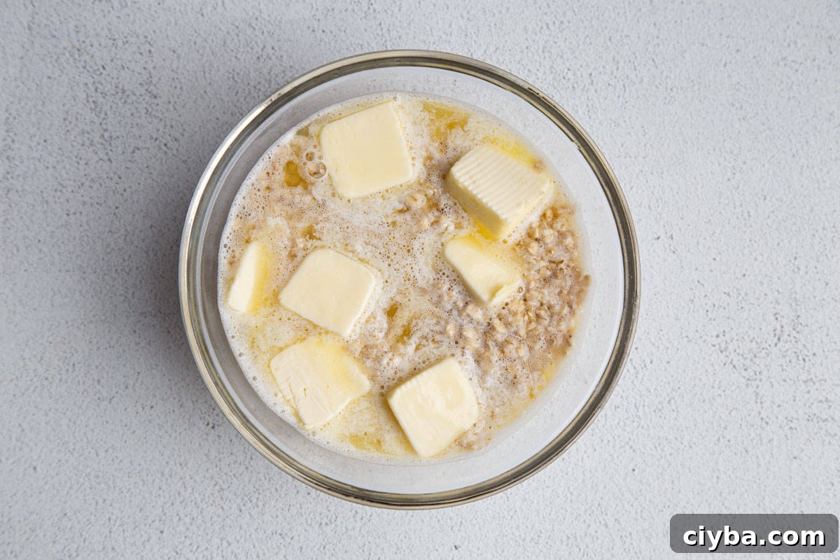 Lazy Daisy Oatmeal Cake Recipe with Cinnamon and Raisins 5 oats and water in a glass bowl with pats of butter.