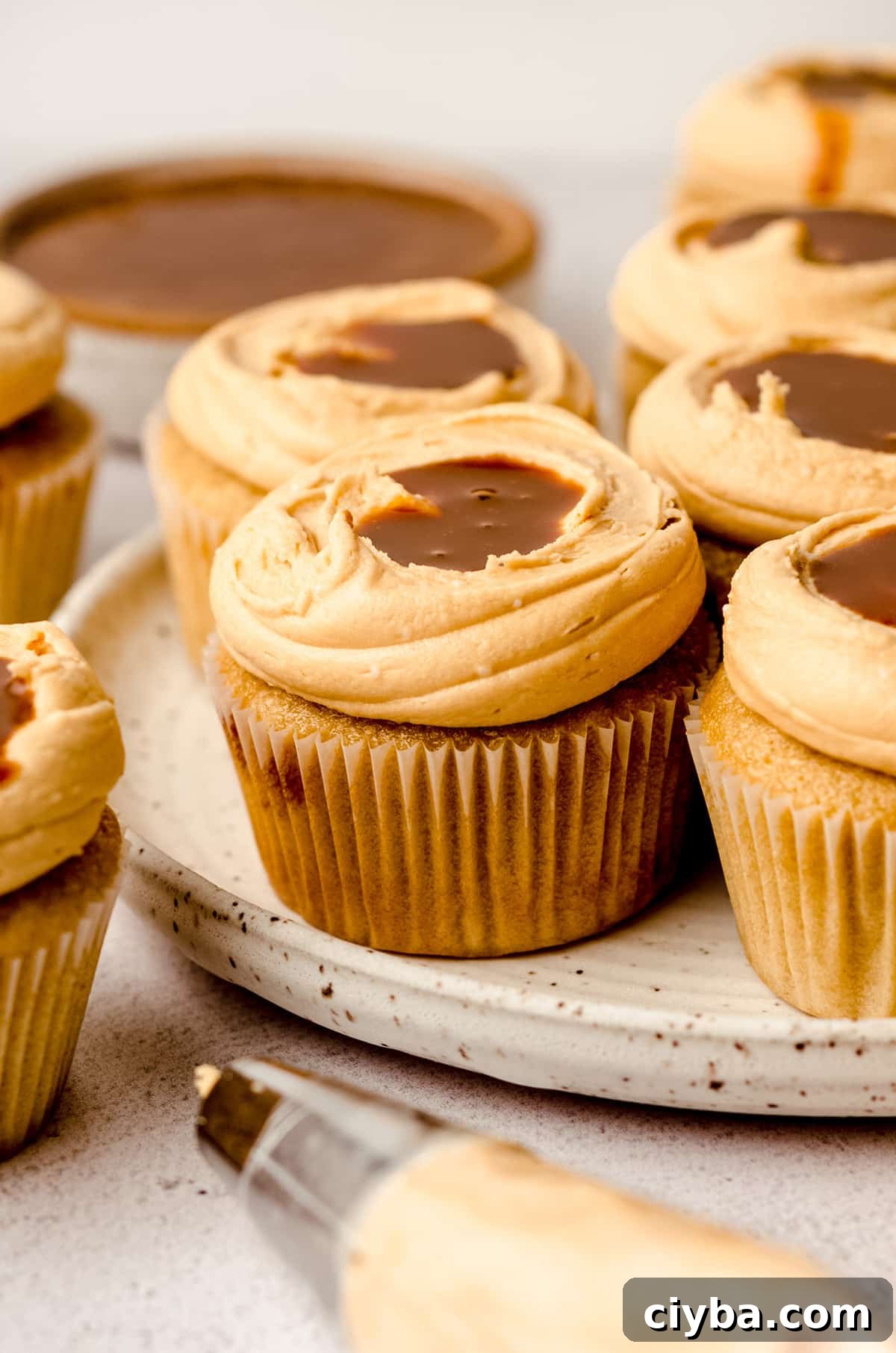 A plate filled with dulce de leche cupcakes, with a piping bag in the foreground.