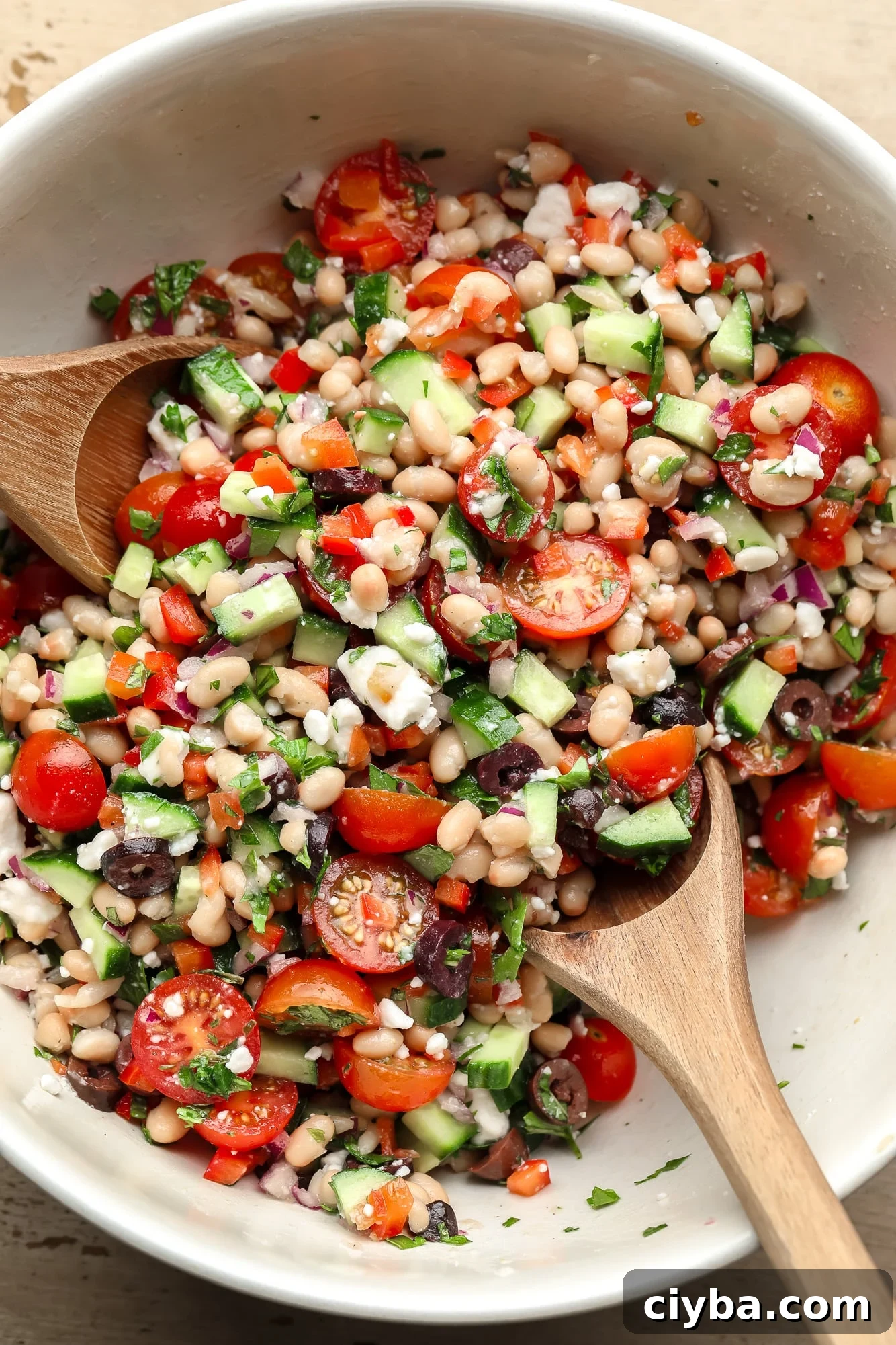using two wooden spoons to toss a white bean salad together.