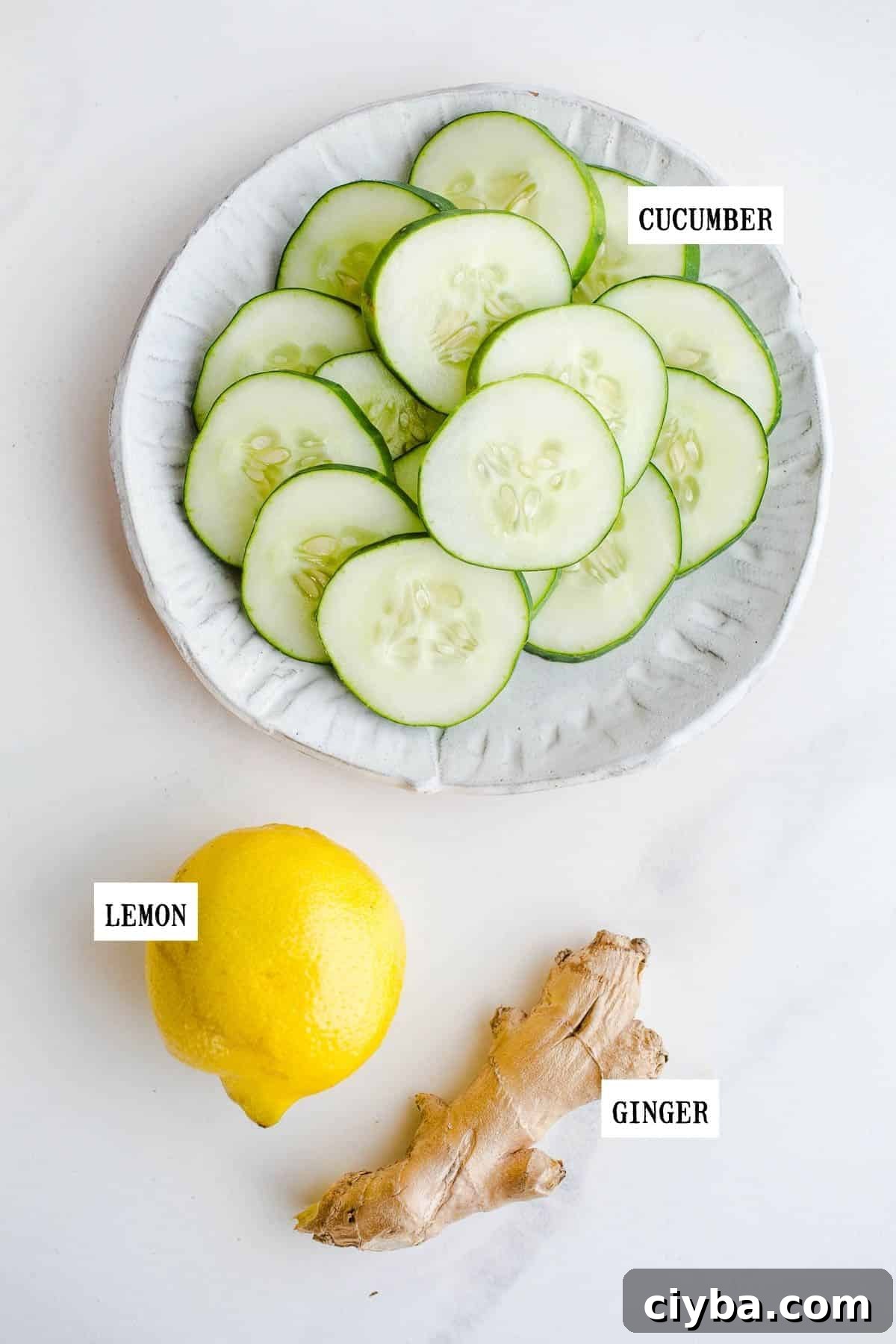 Sliced cucumber, a lemon, and ginger on a marble surface.