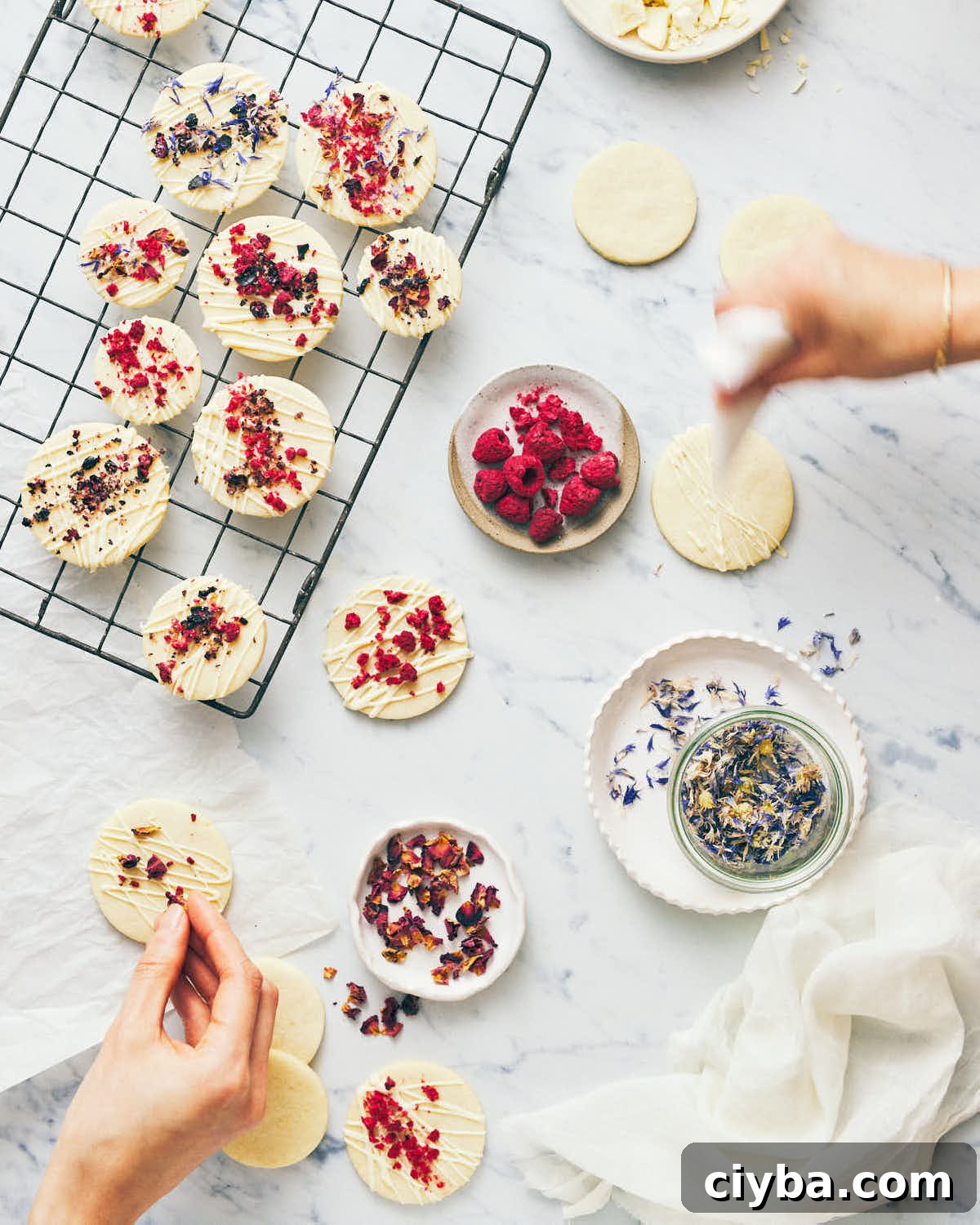 Cookies being iced and topped with dried flowers on a marble surface