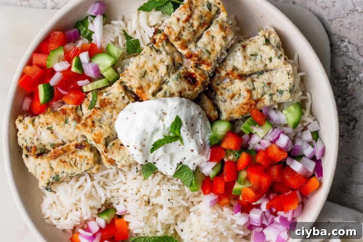 Crispy Air Fryer Mediterranean Chicken Bites with Herbs 2 A bowl of white rice topped with grilled kebab pieces, diced red onion, red and green bell peppers, and a dollop of yogurt garnished with a mint leaf.