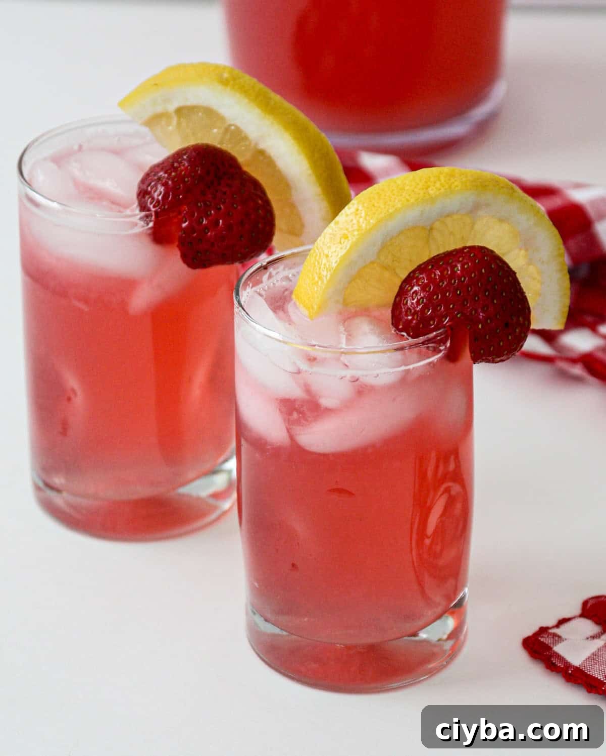 Two glasses of rhubarb lemonade, garnished with lemon and strawberry slices.