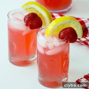 Two glasses of rhubarb lemonade, garnished with lemon slices and strawberries.