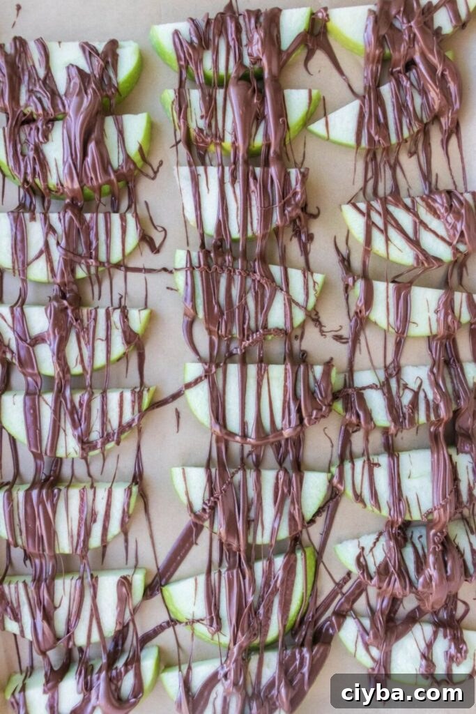 sliced apples on parchment paper drizzled with melted chocolate