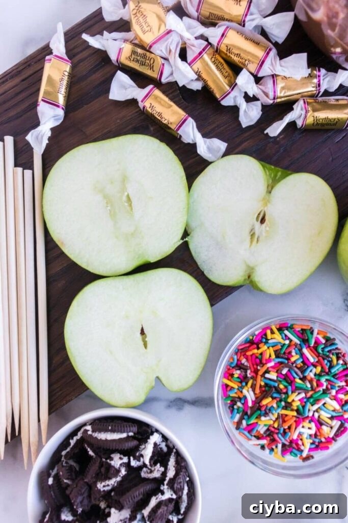 sliced apples on counter with wrapped caramels, and bowls of crushed cookies and sprinkles beside the apples 