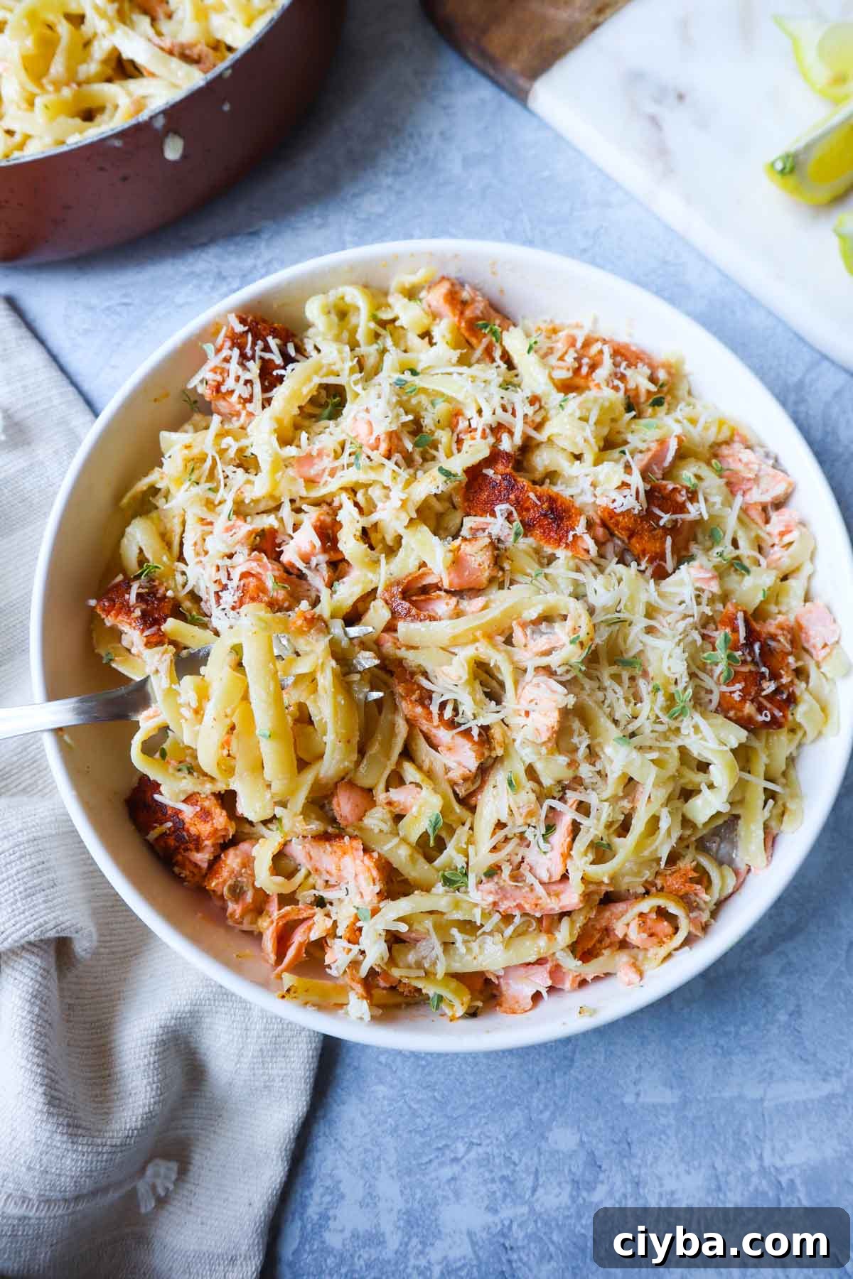 white bowl with fettuccine alfredo topped with parmesan and cajun salmon