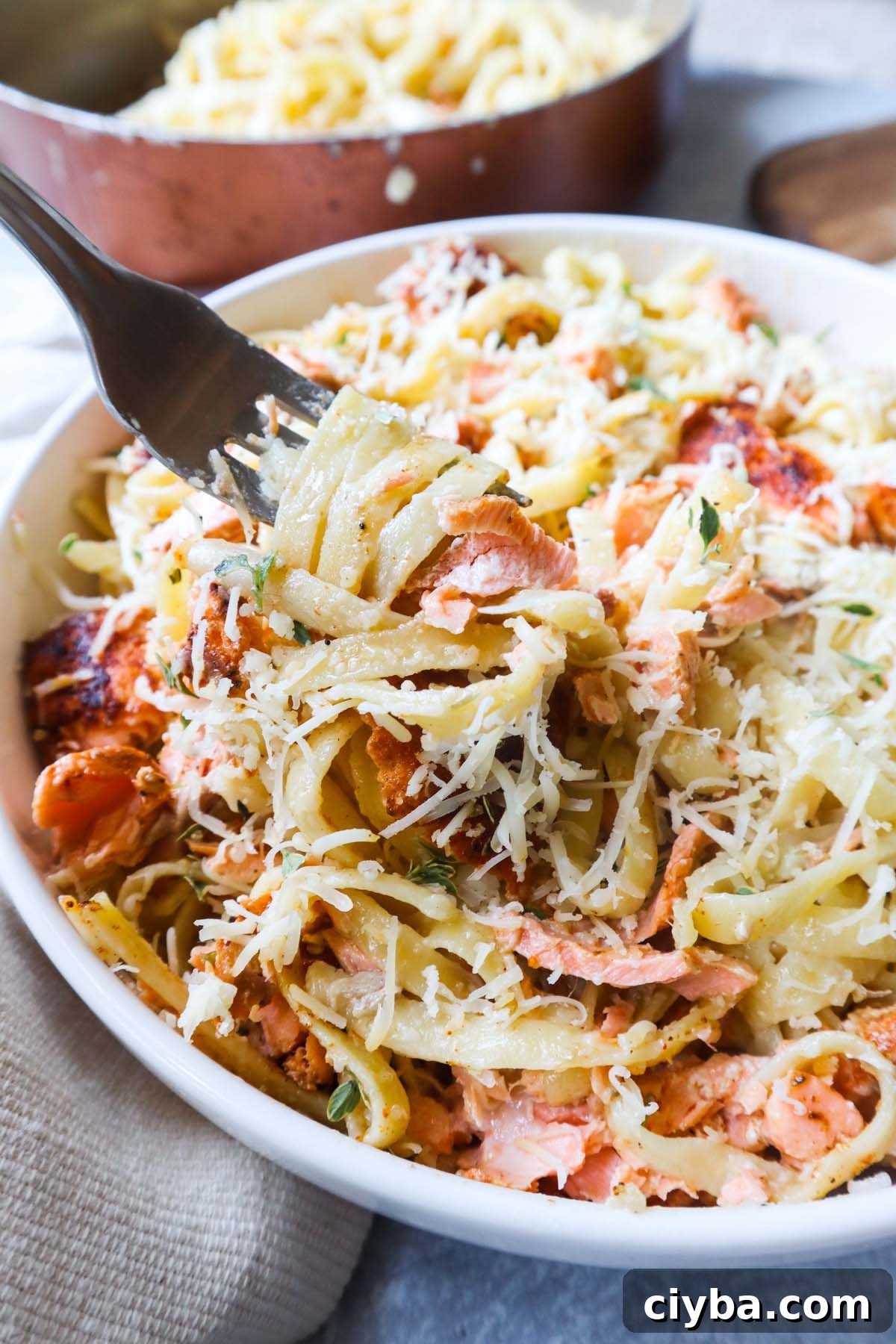white bowl with fettuccine alfredo topped with parmesan and cajun salmon