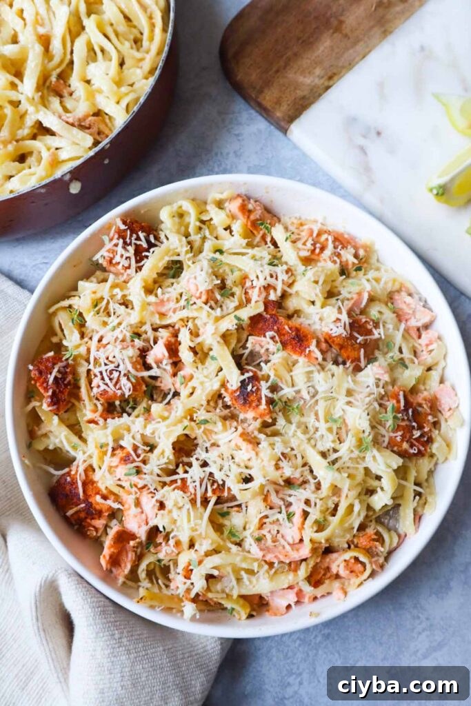 white bowl with fettuccine alfredo topped with parmesan and cajun salmon