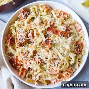 white bowl with fettuccine alfredo topped with parmesan and cajun salmon