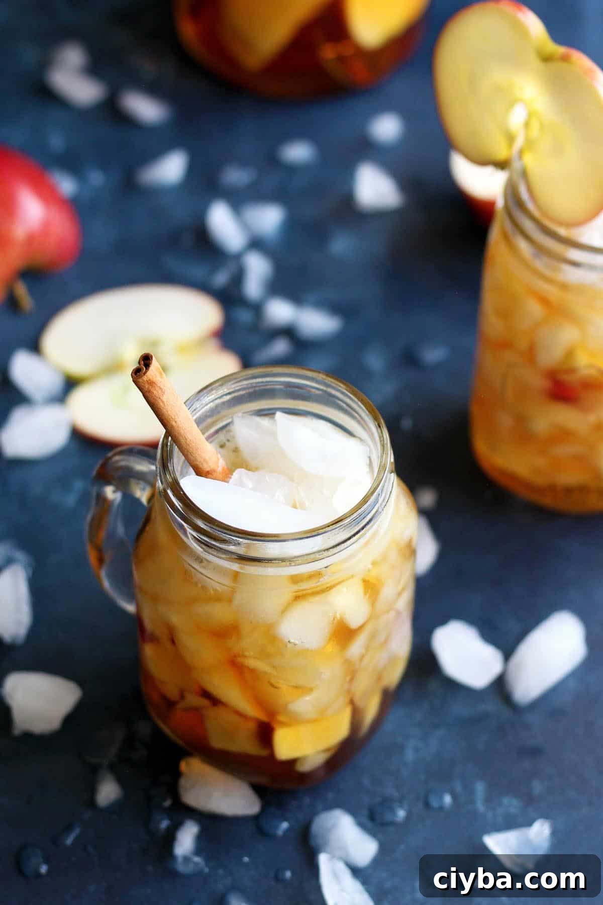 Autumn Pimm’s Cup Cocktail Recipe for Cozy Evenings 4 A couple apple Pimm's cup cocktails on a blue table tops with ice spread all over.