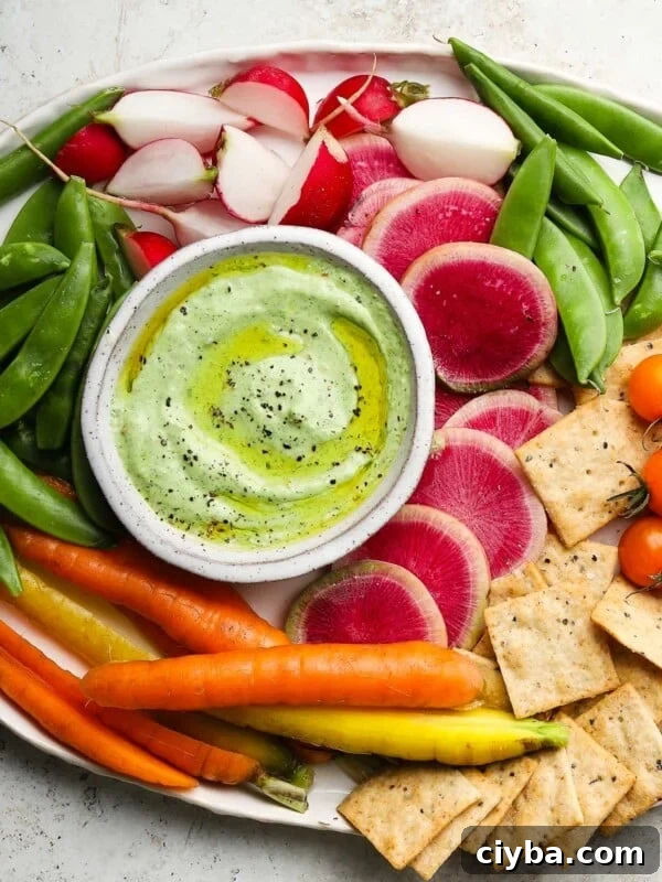 Colorful vegetable platter with green yogurt dip, radishes, snap peas, carrots, and crackers.
