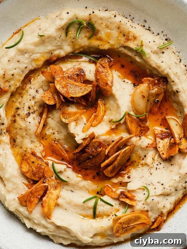 Creamy white bean dip with crispy garlic and fresh rosemary garnish.