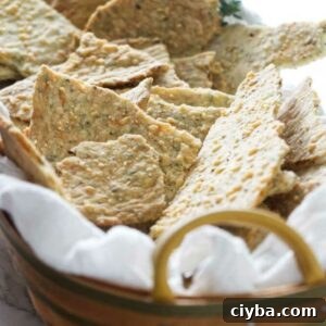 Basket with homemade seeded crackers on white cloth, herbs in background.