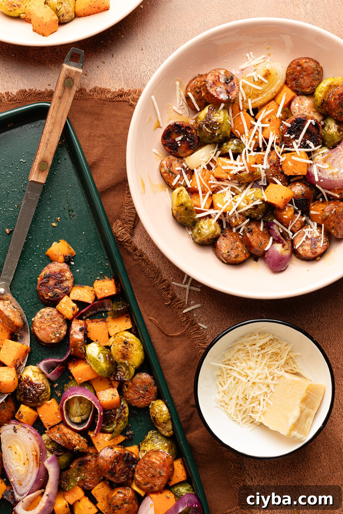 A serving bowl filled with an Autumn sheet pan dinner topped with shredded permesan cheese sitting next to the rest of the sheet pan made with chicken sausage and veggies