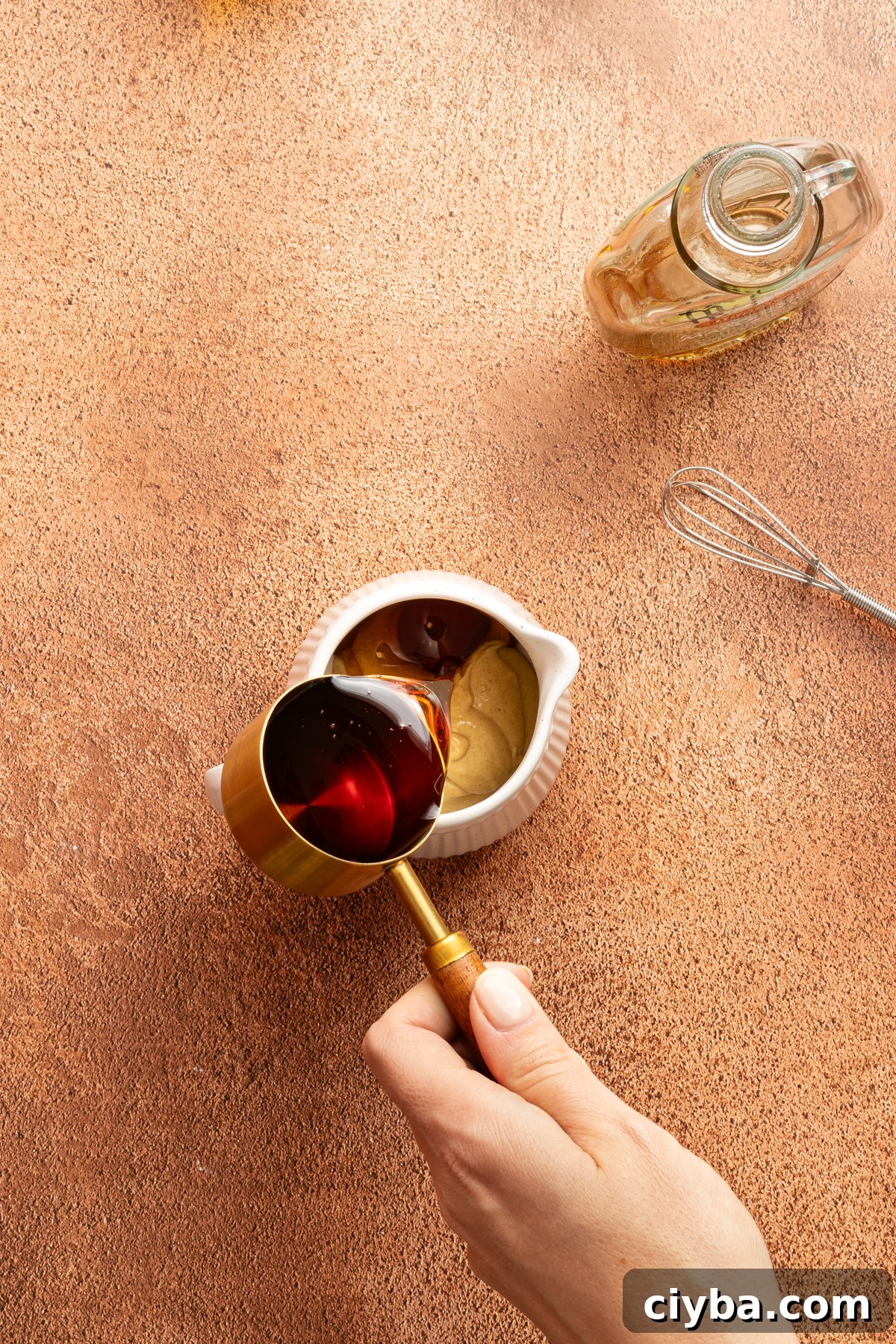 Maple syrup being poured into a small jar with smooth dijon mustard to make a maple-dijon sauce