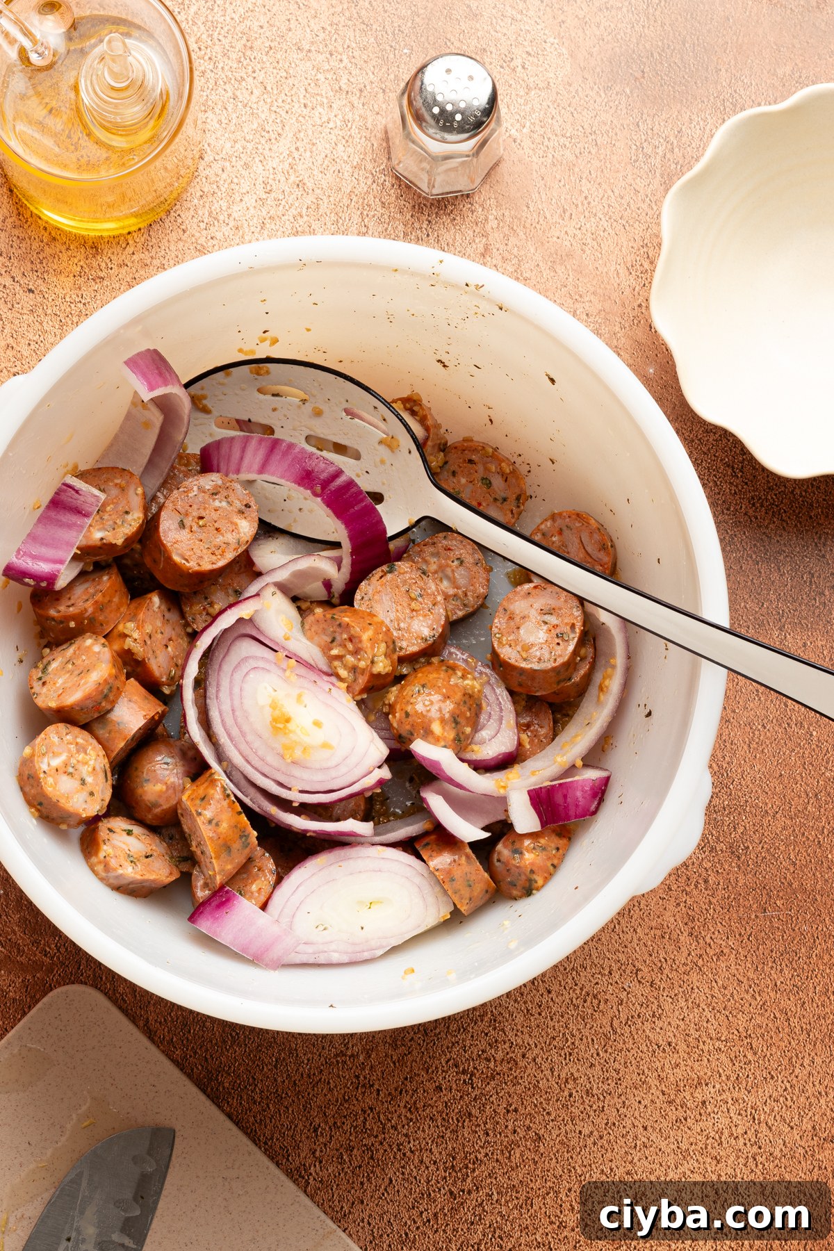 A large white bowl filled with sliced smoked chicken sausage, red onion and garlic mixed together