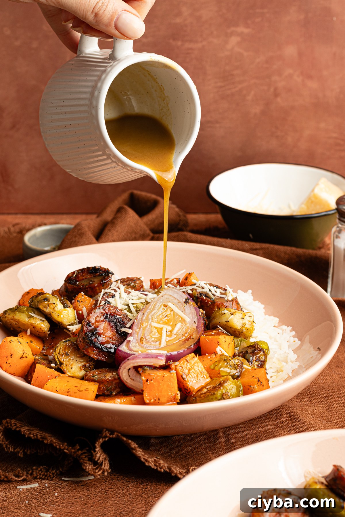 An Autumn sheet pan dinner made with chicken sausage and veggies served over rice and garnish with shredded parmesan and a maple-dijon sauce