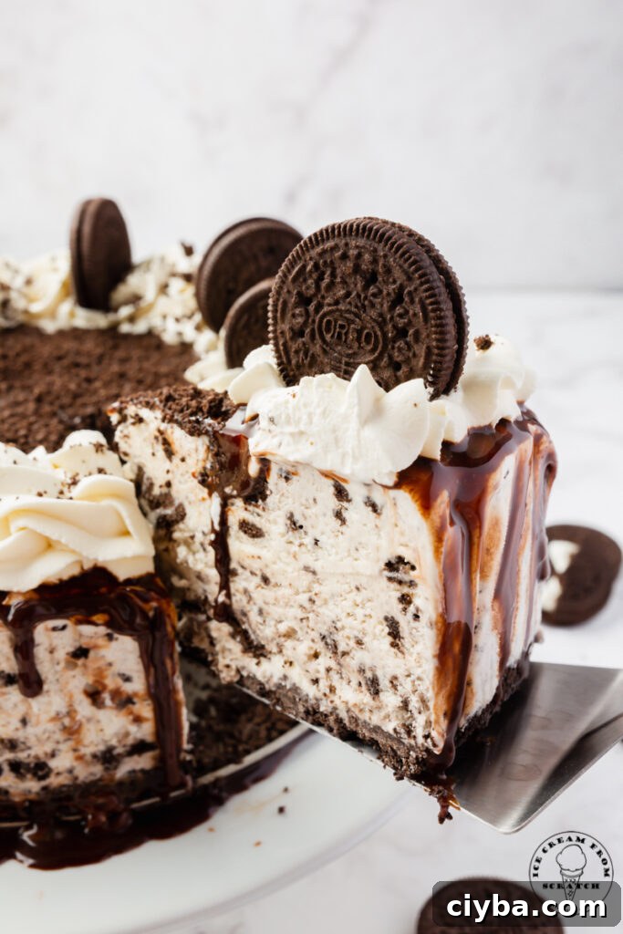 A slice of Oreo Ice cream cake, being lifted away from the full cake with a cake server.