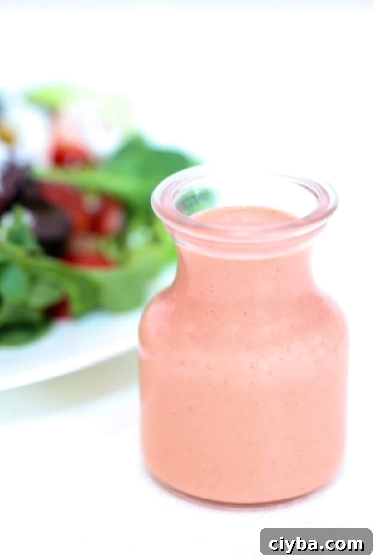 Strawberry Balsamic Salad Dressing in a glass dressing jar with a salad in the background.