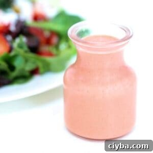 Strawberry balsamic vinaigrette in a glass jar with a salad in the background.