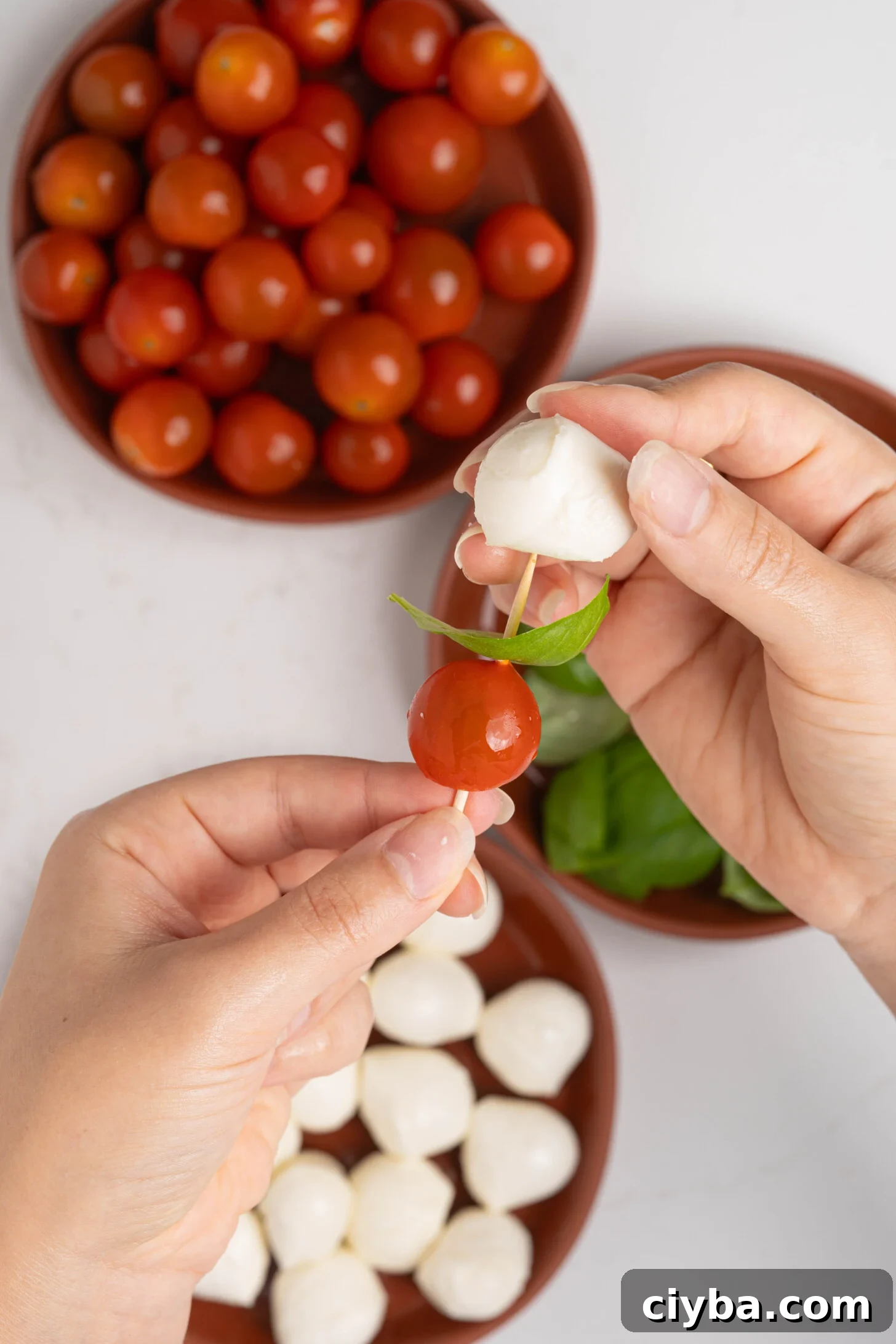 Caprese Skewers with Balsamic Glaze — Tomato, Mozzarella & Basil 5 Hands skewering caprese salad on toothpicks.