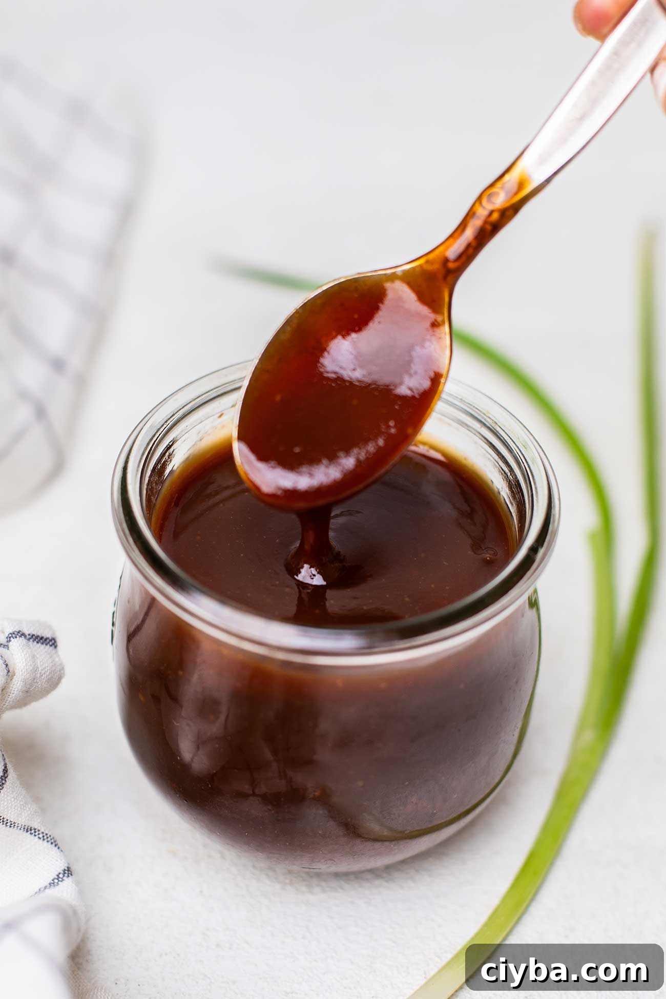 A spoon drizzling some honey bbq sauce out of a jar.