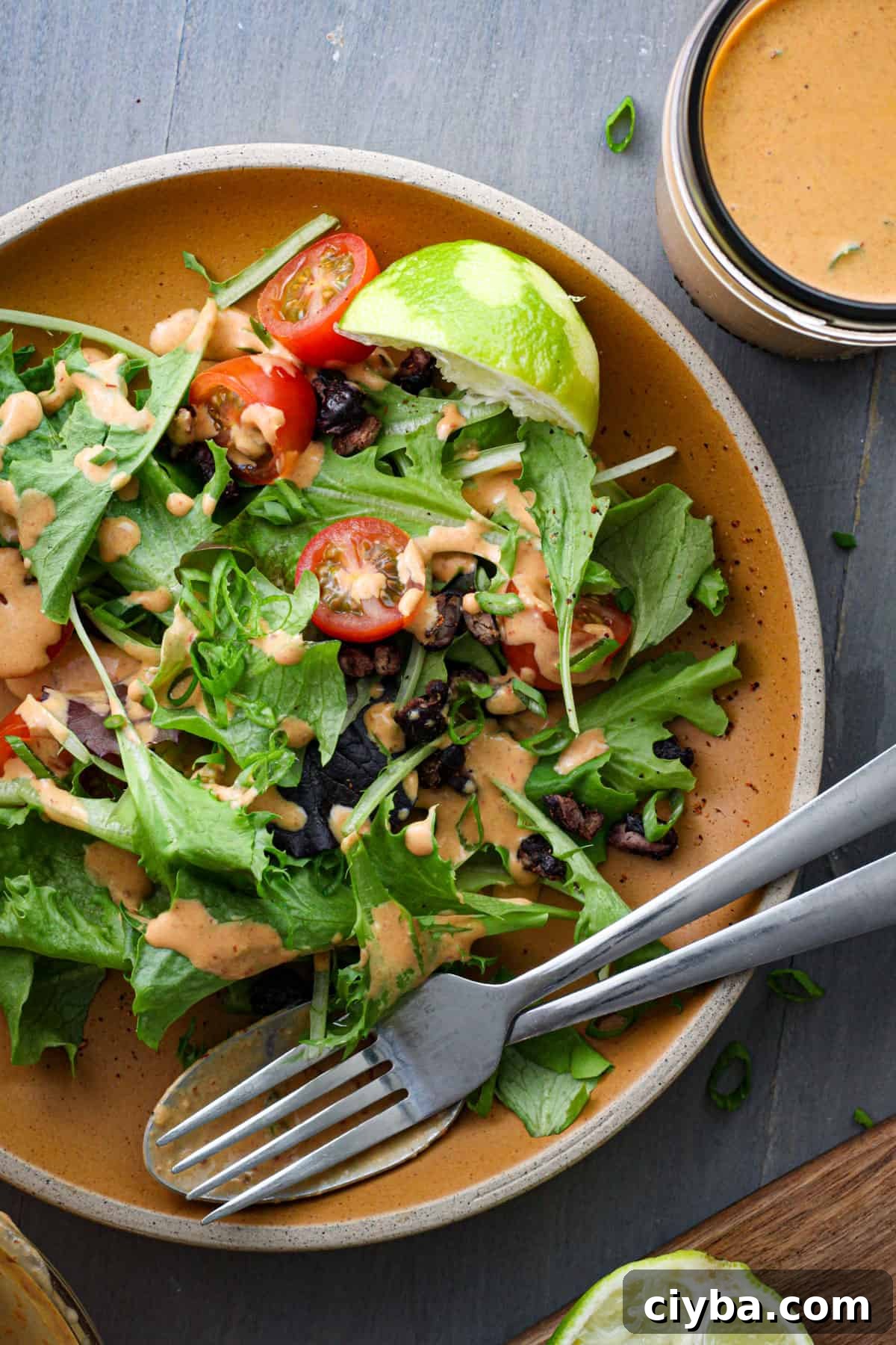 A green salad topped with creamy chipotle lime sauce, chopped tomatoes, lime wedges and roasted black beans.
