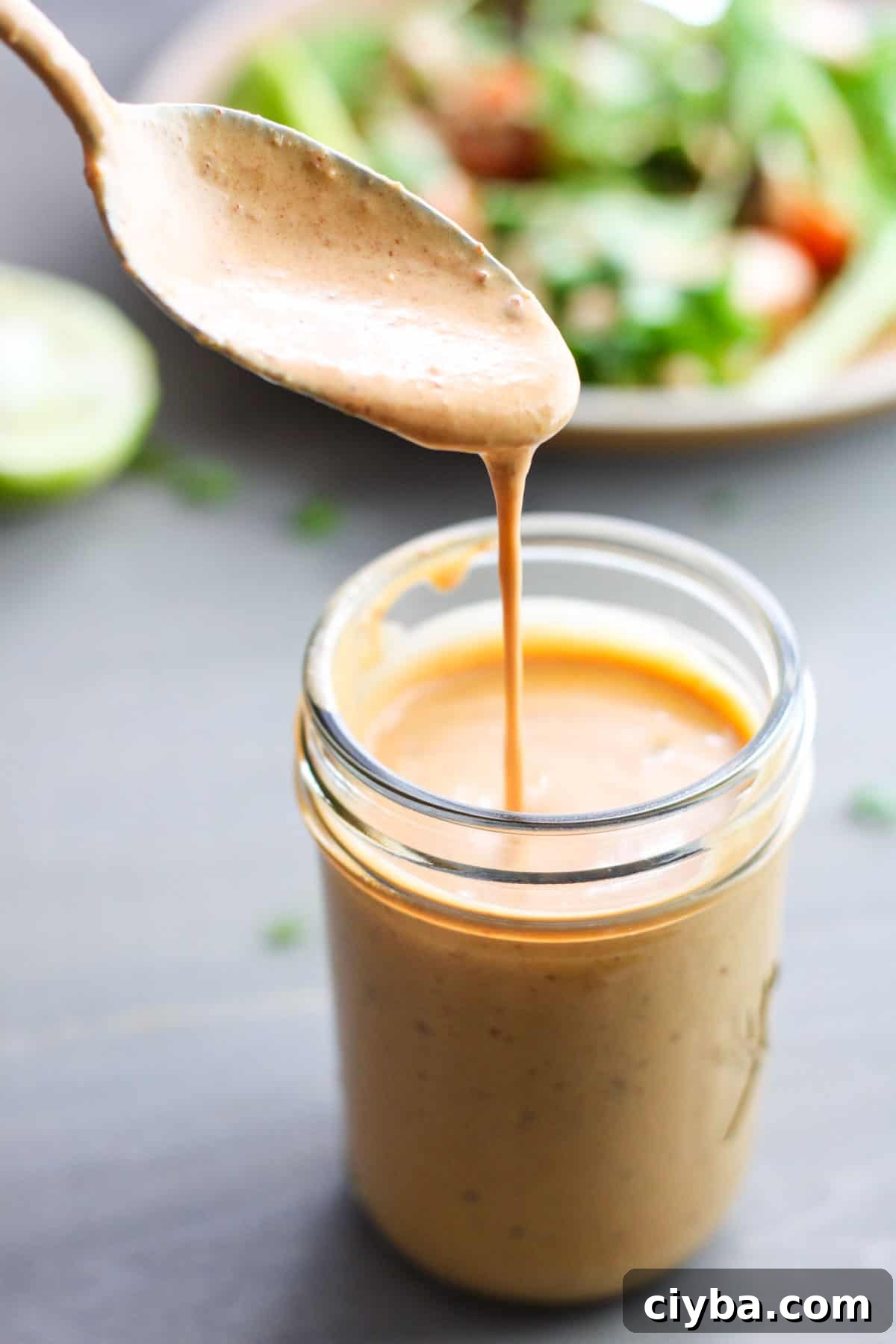 A spoon drizzling creamy chipotle lime sauce into a jar.
