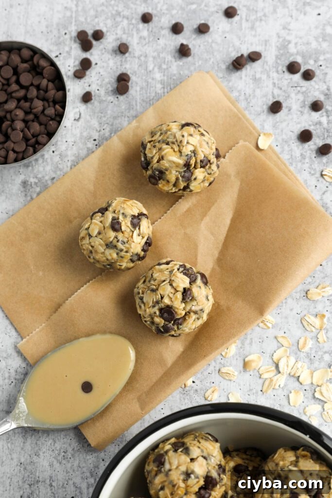 Tahini Chocolate Chip Bliss Balls on top of parchment paper with chocolate chips and oats scattered and spoon of tahini 