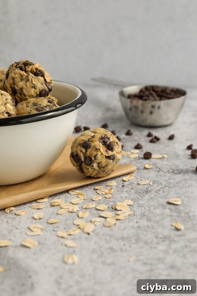 Tahini Chocolate Chip Bliss Balls served in bowl on top of parchment paper with chocolate chips and oats scattered and spoon of tahini 
