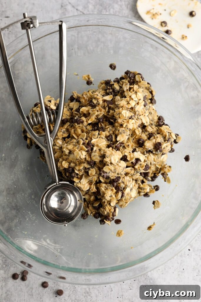 Tahini Chocolate Chip Bliss Ball dough in bowl with cookie scoop and scattered chocolate chips