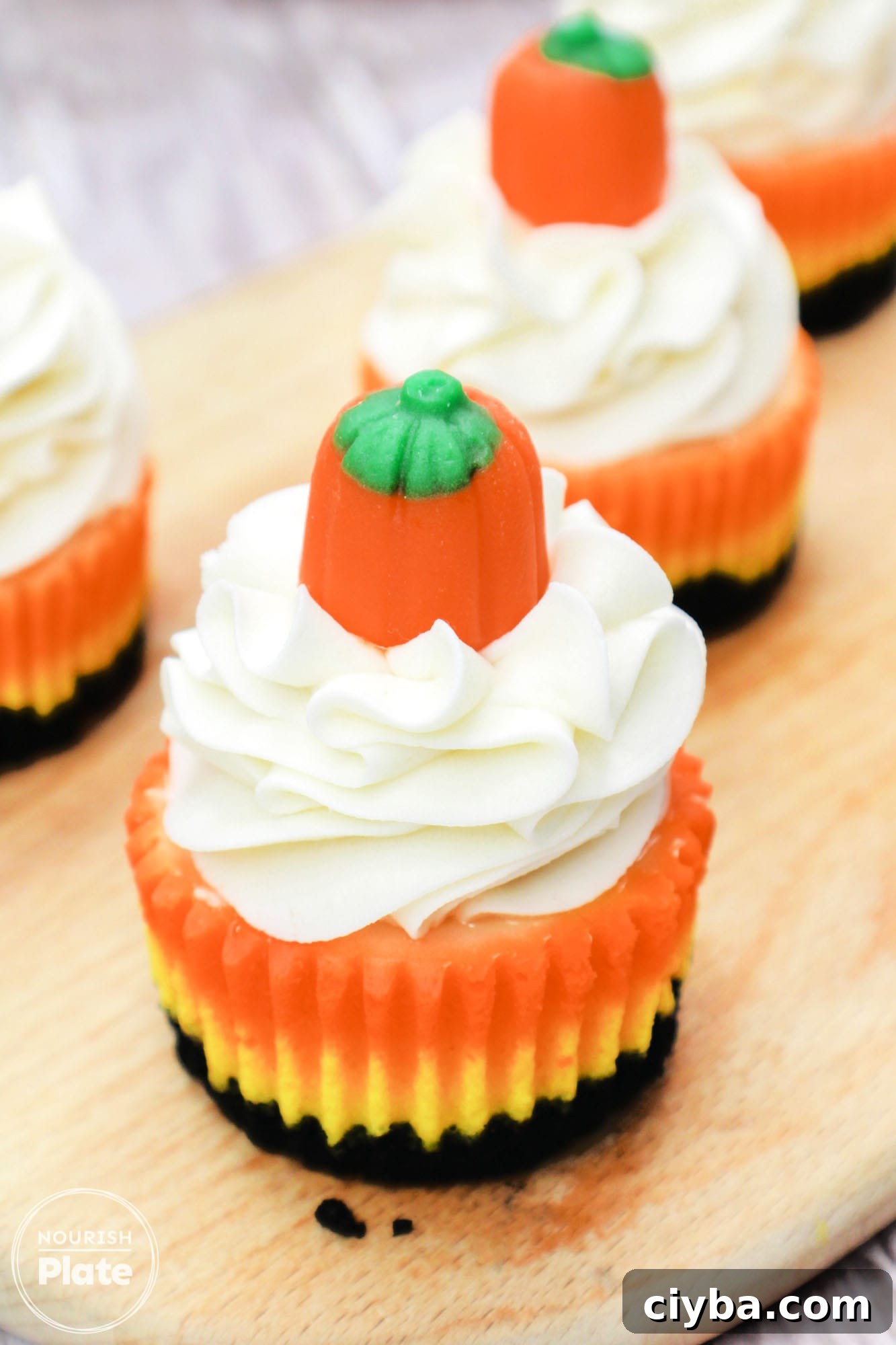 Mini candy corn cheesecake topped with whipped cream and a candy pumpkin