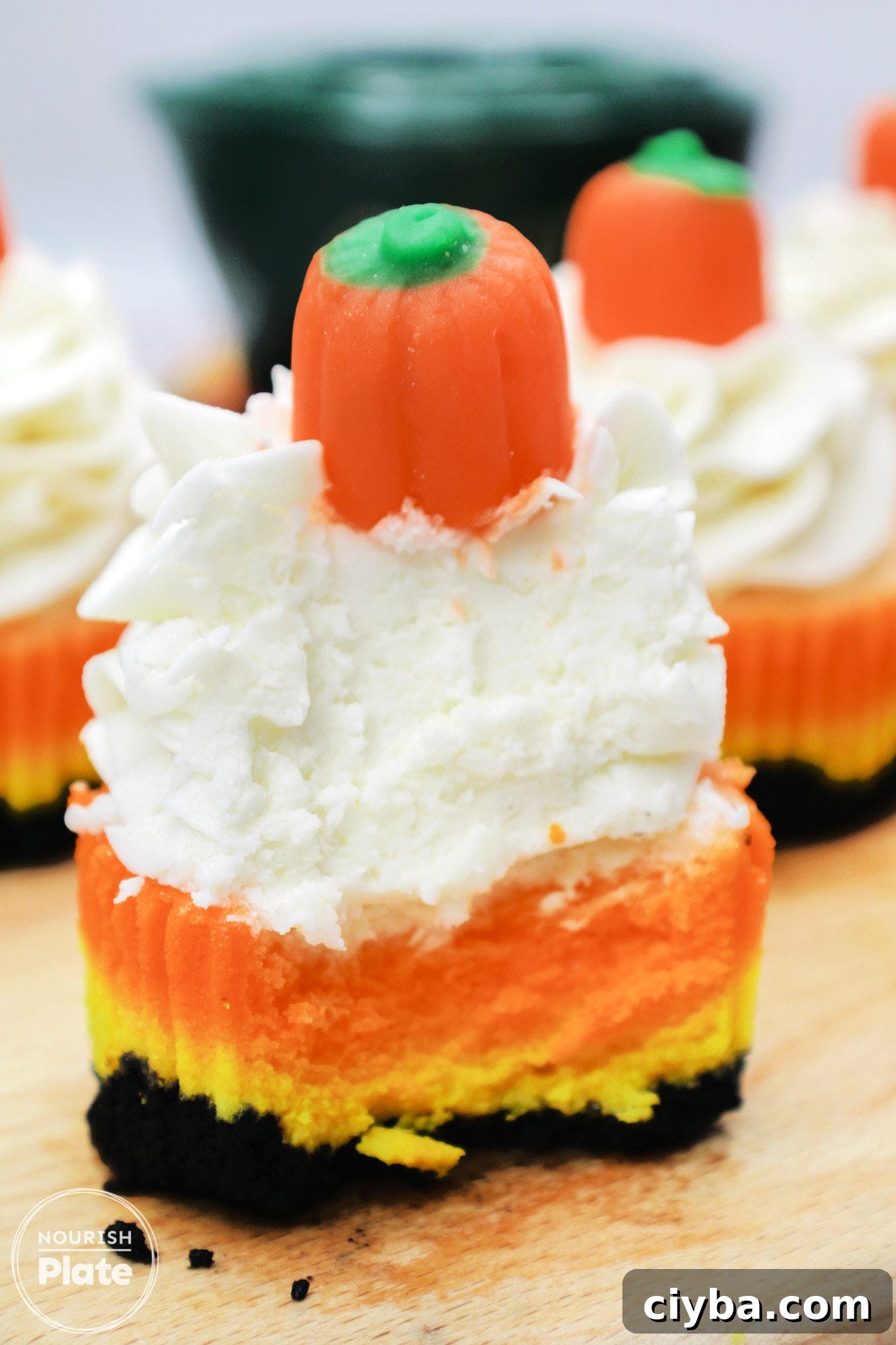A bite shot of a candy corn mini cheesecake topped with whipped cream and candy pumpkin