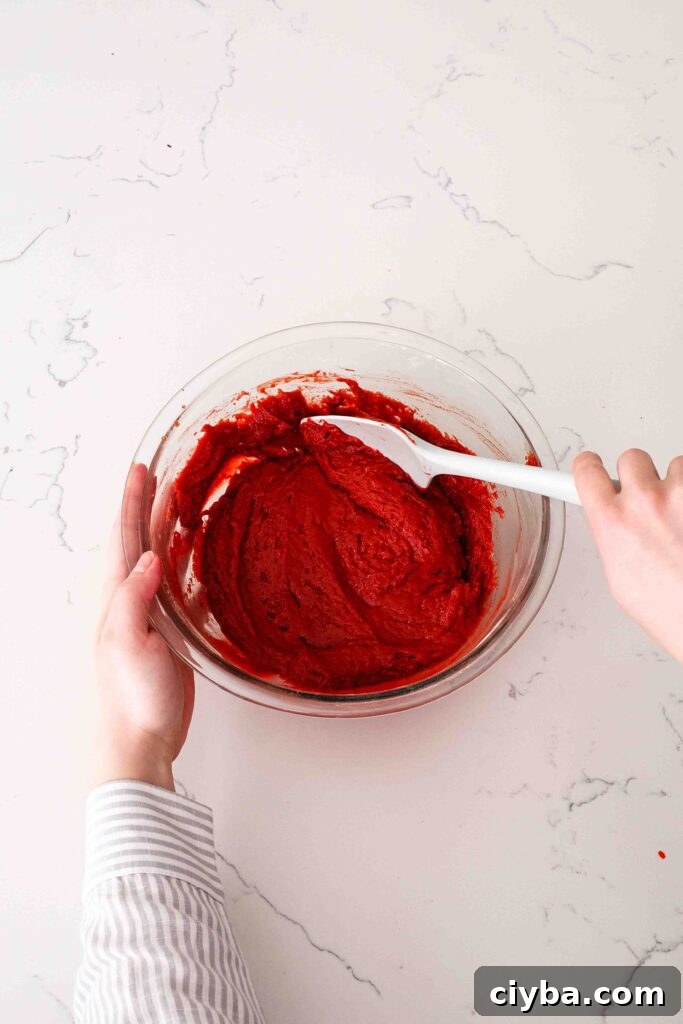Red Velvet Cupcakes with Cream Cheese Frosting Recipe 6 Two hands fold together the red velvet cake batter in a glass bowl.