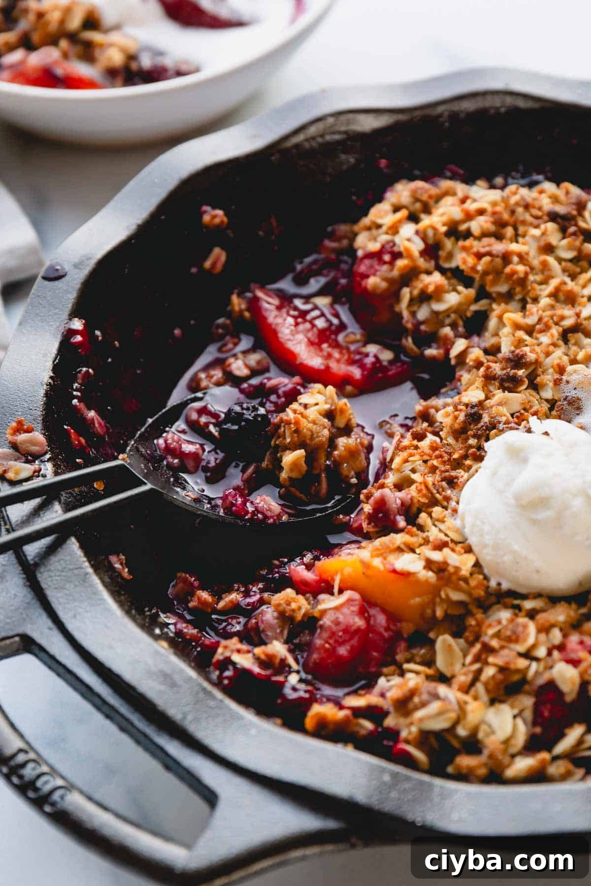 A spoon scooping up a portion of easy fruit crisp topped with vanilla ice cream.