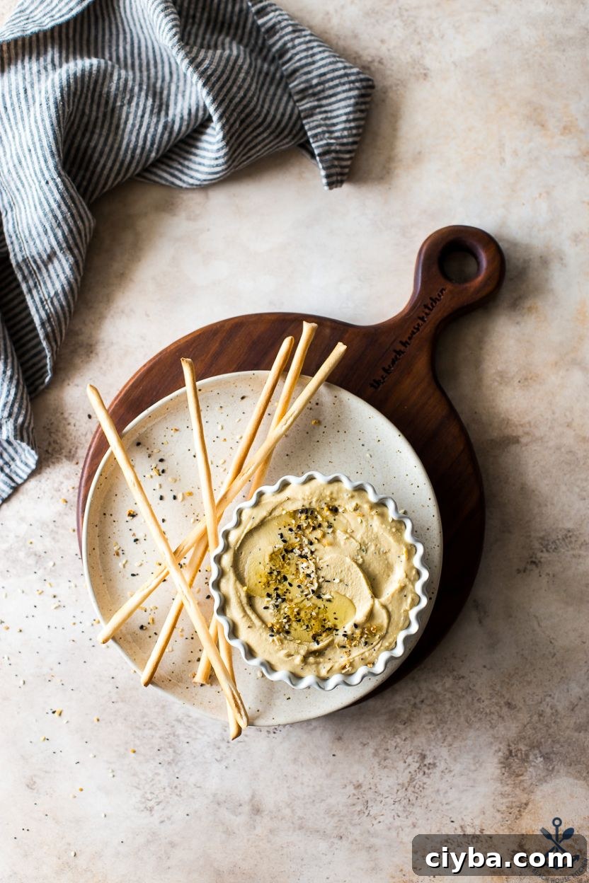 Overhead photo of a dish of hummus on a plate with thin breadsticks