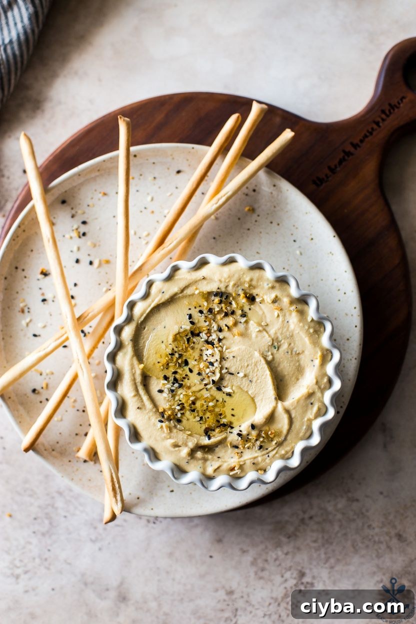 Up close overhead photo of everything hummus in a bowl on a plate with thin breadsticks