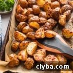 Crispy Parmesan-Crusted Red Potatoes for Dinner 9 A parchment-lined sheet pan filled with roasted Parmesan crusted red potatoes, being tossed with a saute tool.
