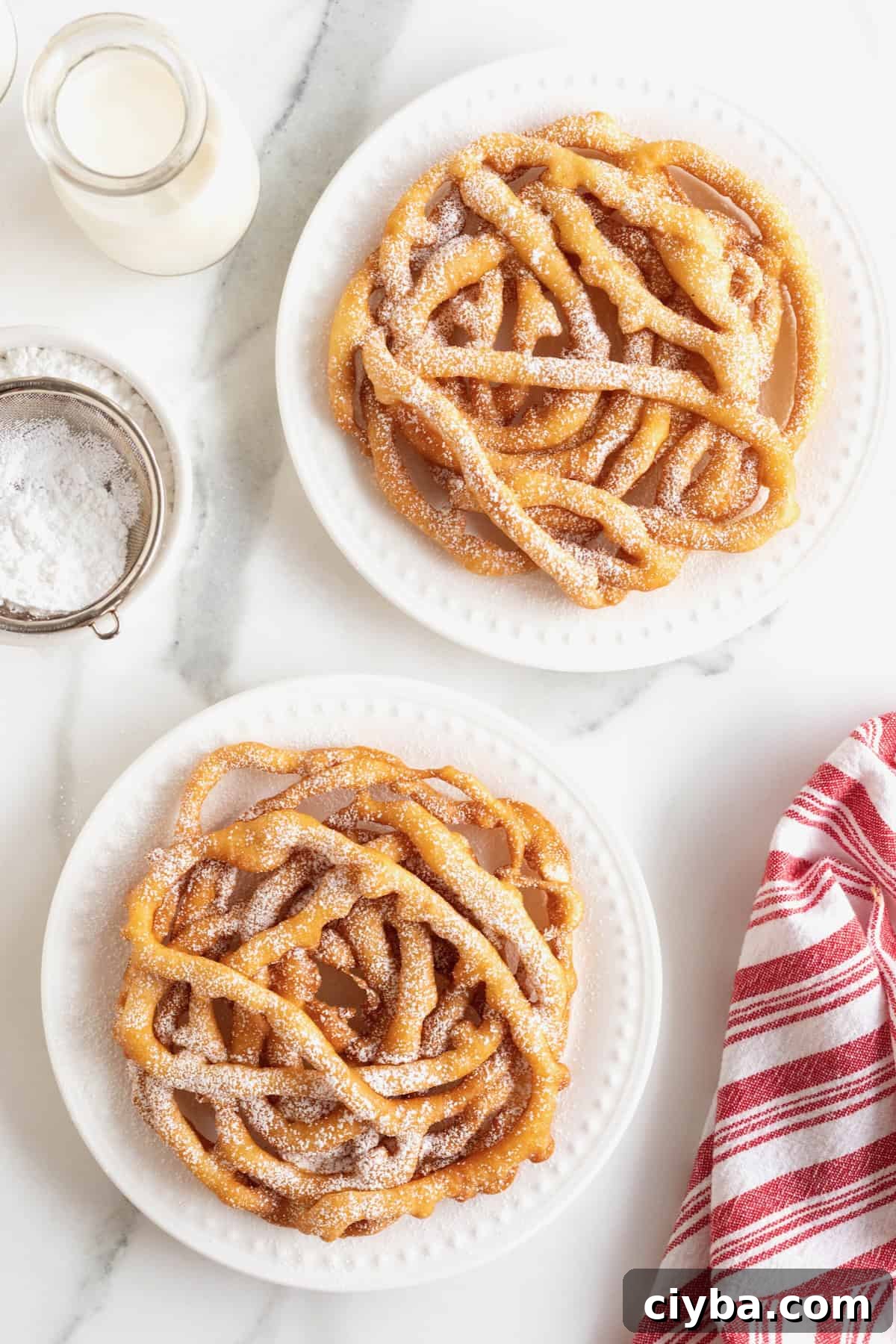 Two funnel cakes topped with powdered sugar on white plates.