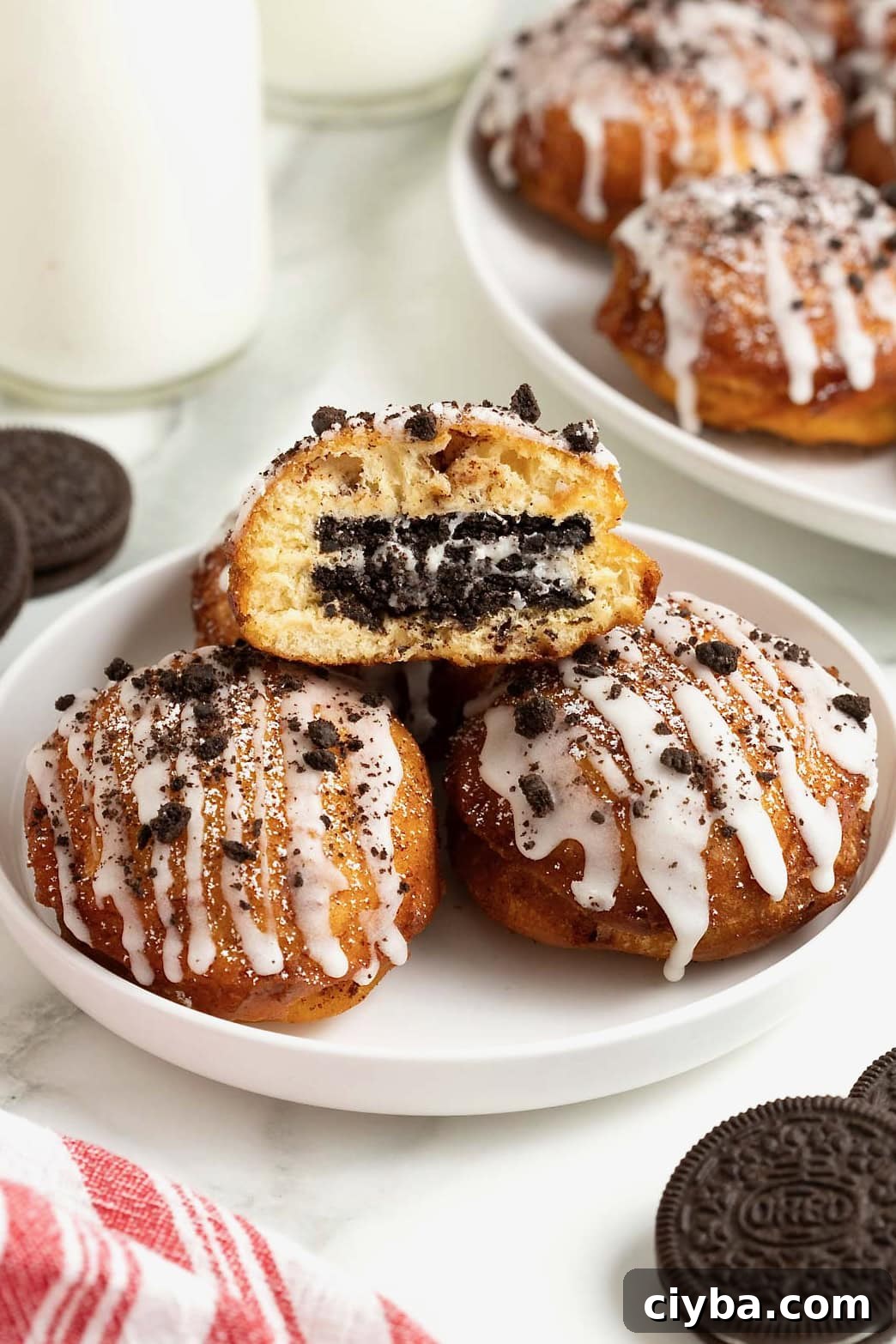 A white rimmed plate holding three fried cinnamon rolls with Oreos in the middle. The one of top is cut open to reveal the oreo inside.